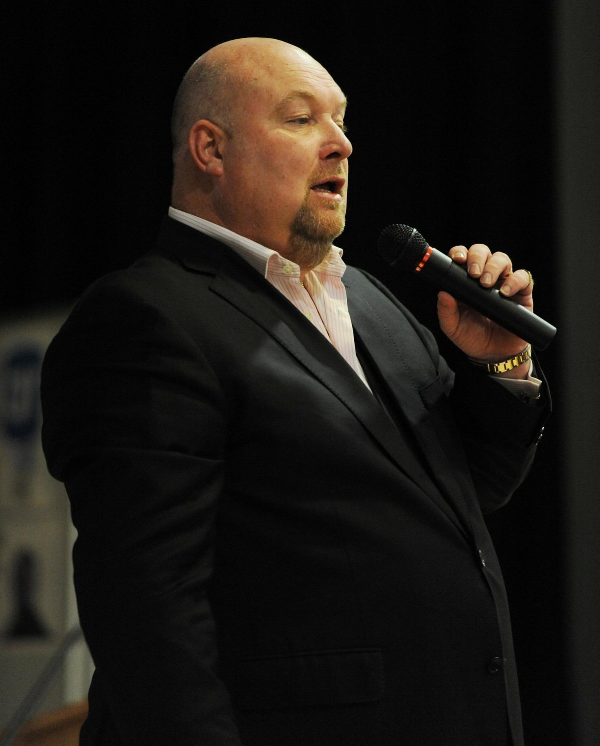 John Pridmore speaking into a microphone on a darkened stage